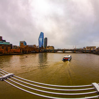 Millennium Bridge over the River Thames near Blackfriars in London, England, with boats cruising along the river and the city skyline in the background